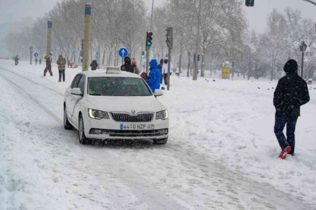 Une voiture arrêtée sur une route enneigée, avec deux personnes marchant dans la neige, illustrant les conditions hivernales difficiles.